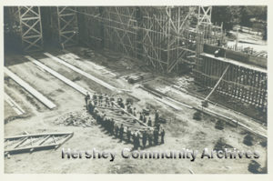 Over thirty men carry a single wooden support structure during the construction of the Arena. 1936
