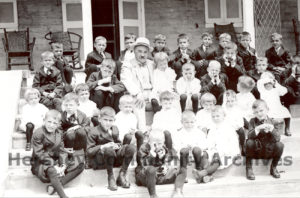 Milton Hershey surrounded by Hershey Industrial School students, seated on the steps of The Homestead, 1913