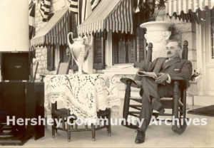 Milton Hershey pictured on front porch of High Point with a loving cup from the 10th anniversary celebration of Hershey, 1913