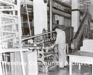 In 1956 Hershey Chocolate Corporation began manufacturing its own tins for Hershey’s syrup. Here an employee monitors the progress of a can labeler. ca. 1960-1970